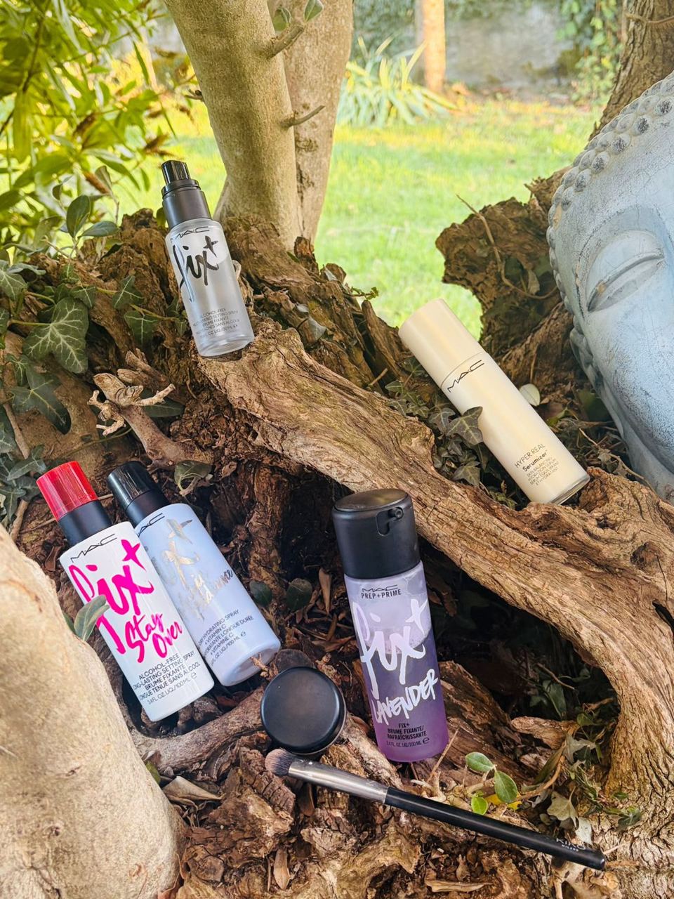 Fijadores, prebase y pincel de maquillaje colocados sobre un tronco en el jardín